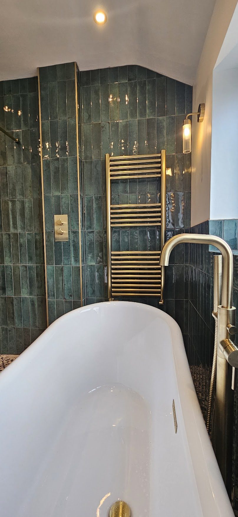 Green tiled bathroom with a freestanding bath and brass fittings