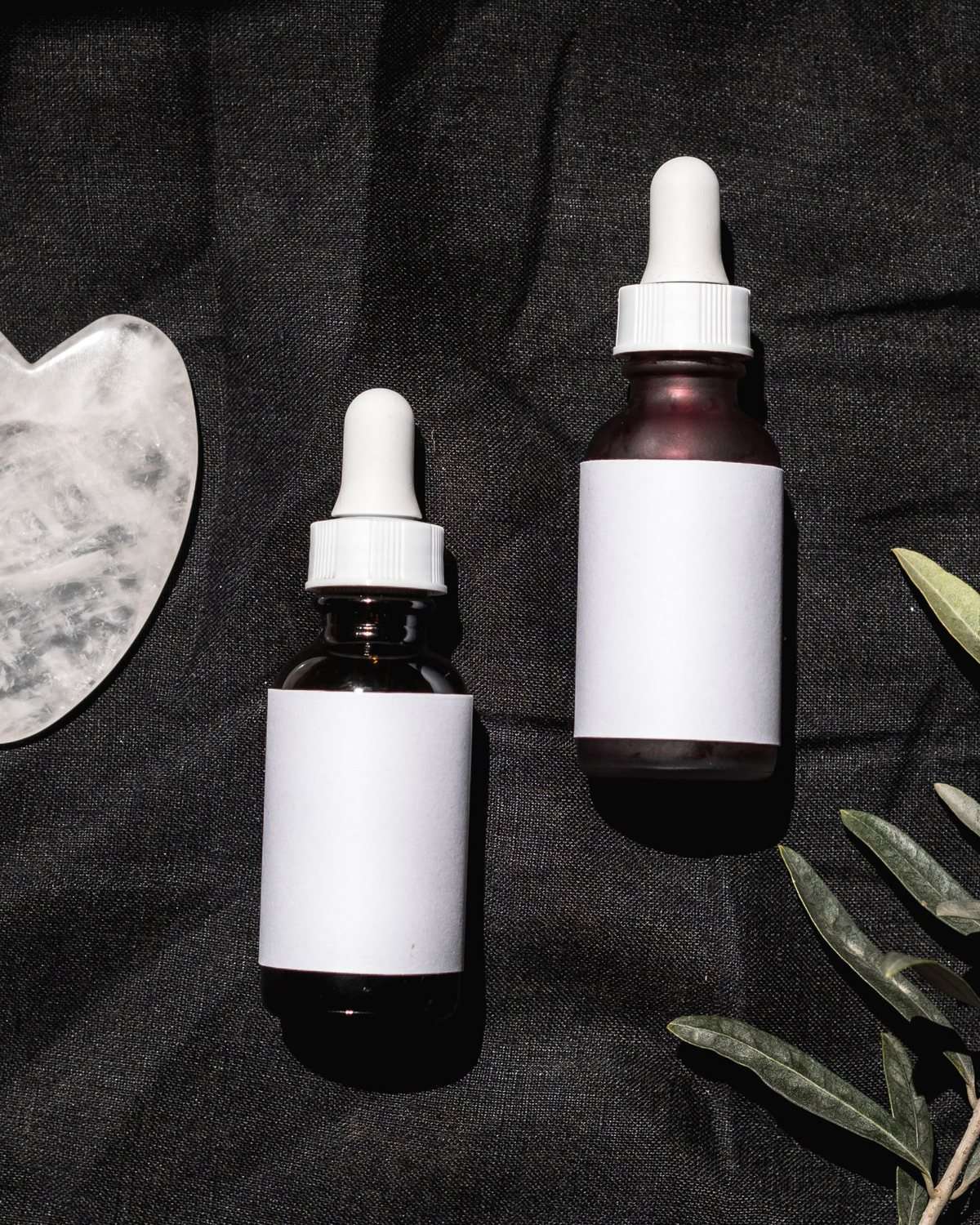 Gua sha stone and treatment serums laid out on dark linen